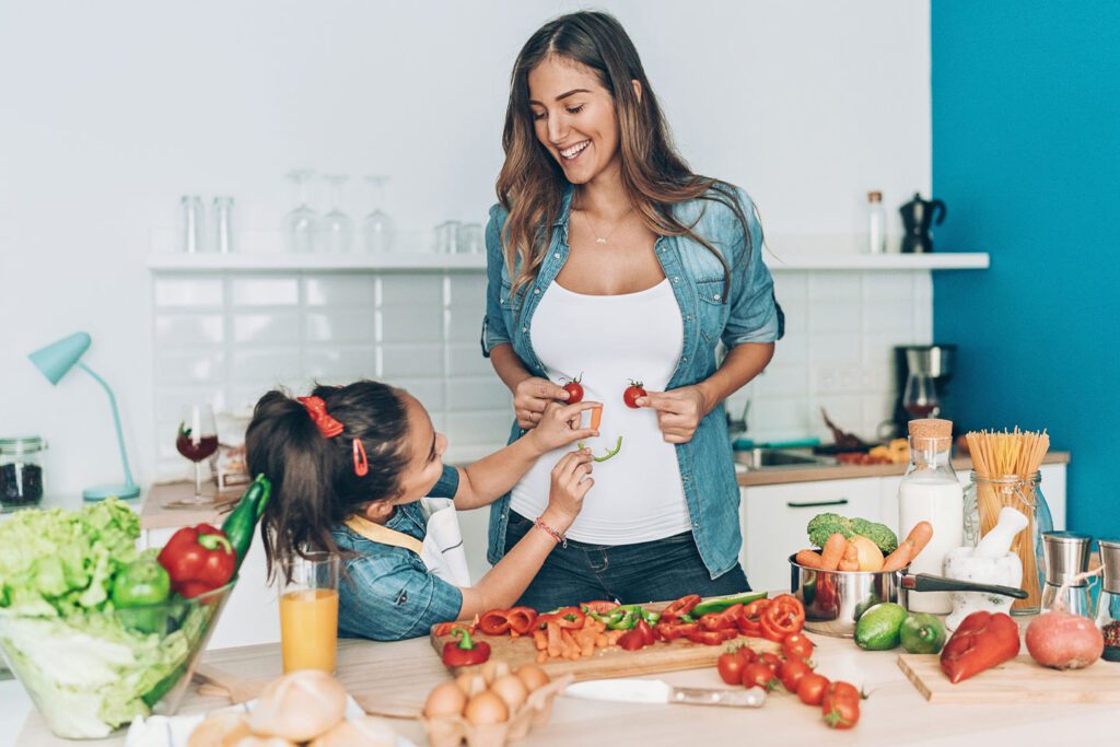 Little girl making a smiley face out of vegetables on her moms stomach to show off good gut health.