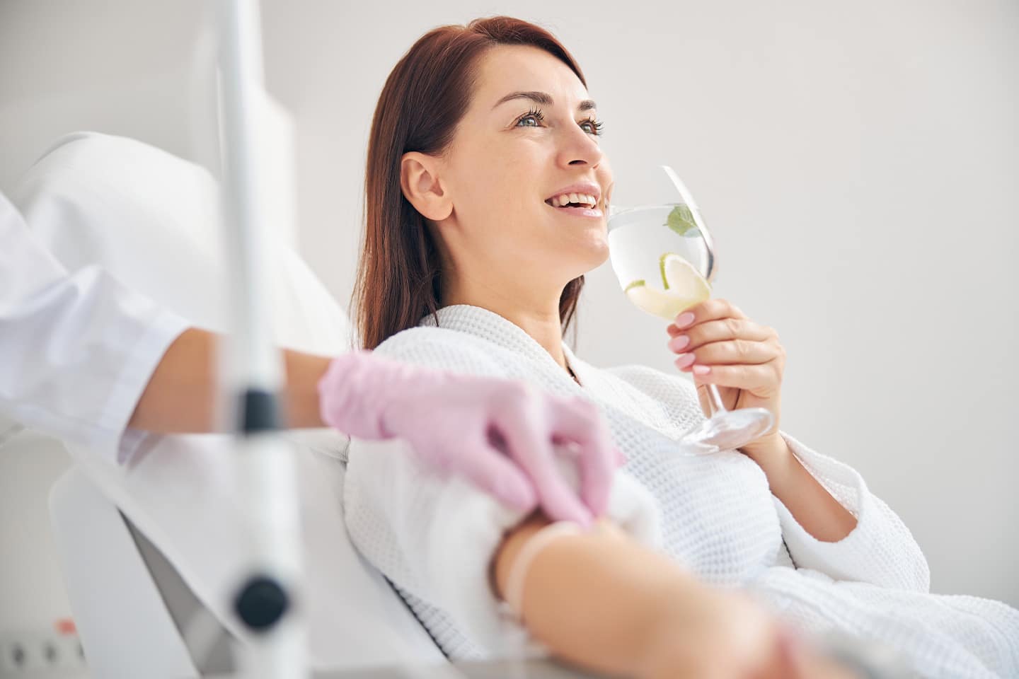 Woman enjoying a cucumber water while getting IV hydration therapy.