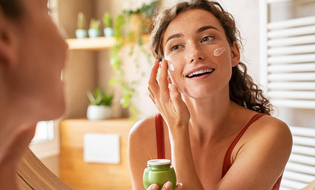 Woman applying medical grade moisturizer in the mirror.